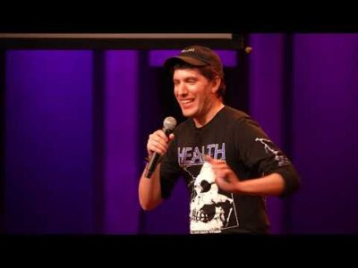 A man wearing a black shirt and hat holds a microphone in his hand.