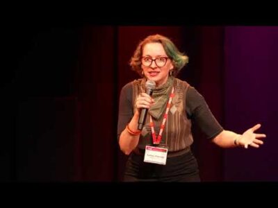 Photo of a woman speaking with a microphone in hand.
