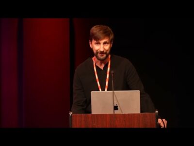 A man delivering a speech at a podium with a laptop displaying visual aids.